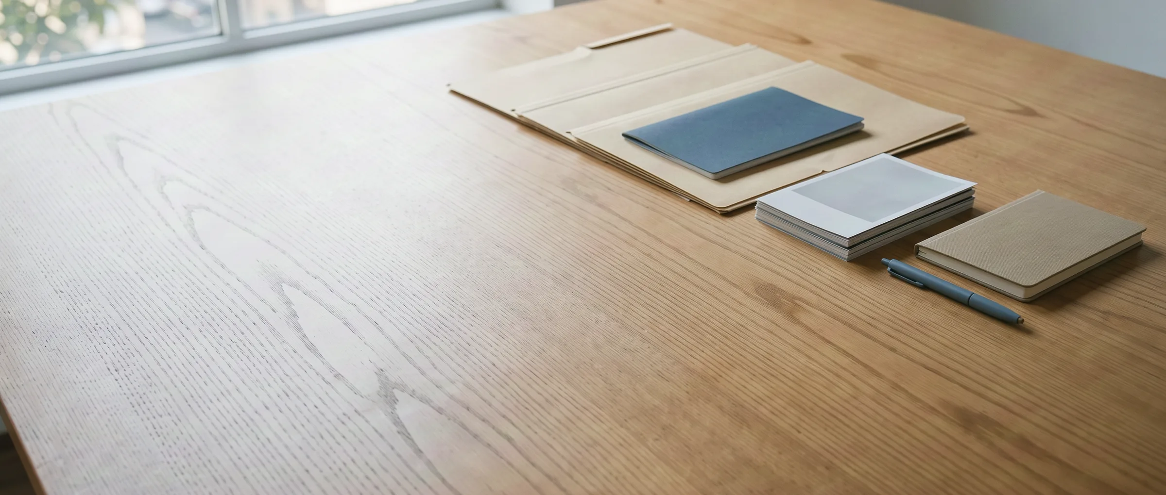 Carpetas, una libreta y un bolígrafo ordenados sobre una mesa de madera clara