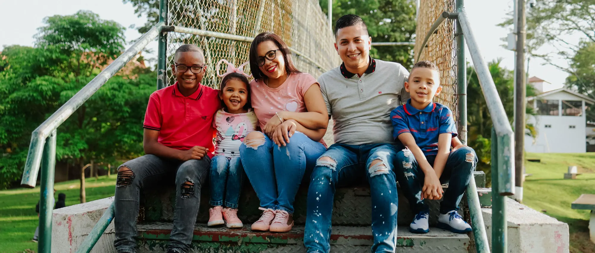 Familia de cinco integrantes sentada junta al aire libre